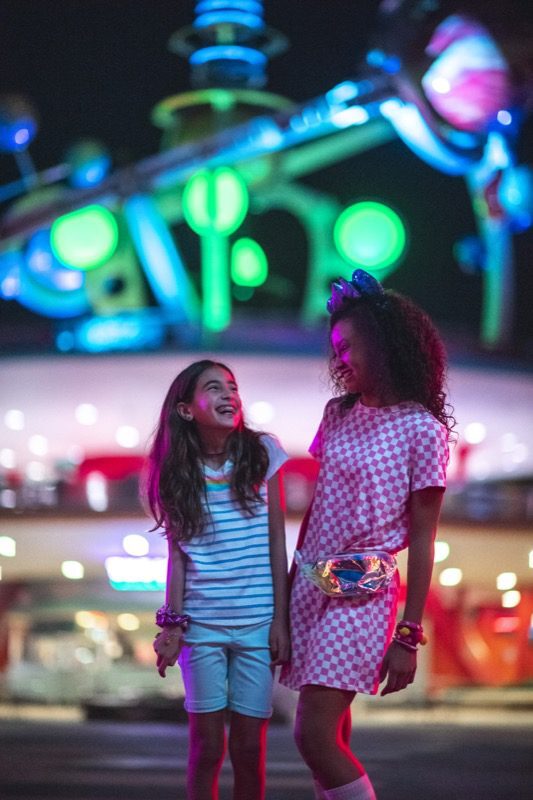Two young girls exploring a brightly lit Disney park at night